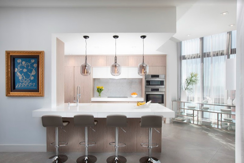 Example of a mid-sized trendy galley porcelain tile and gray floor eat-in kitchen design in Miami with an integrated sink, flat-panel cabinets, light wood cabinets, solid surface countertops, multicolored backsplash, marble backsplash, stainless steel appliances and white countertops