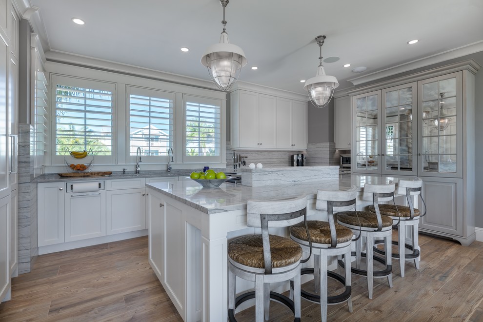 This is an example of a large coastal grey and white kitchen in Tampa with white cabinets, granite worktops, stone slab splashback, integrated appliances, an island, grey worktops, shaker cabinets, multi-coloured splashback and light hardwood flooring.