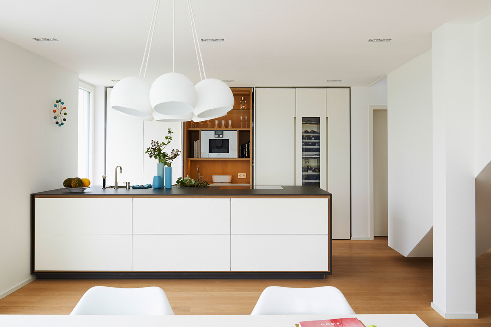 Photo of a medium sized contemporary kitchen/diner in New York with flat-panel cabinets, medium hardwood flooring, an island, an integrated sink and stainless steel appliances.