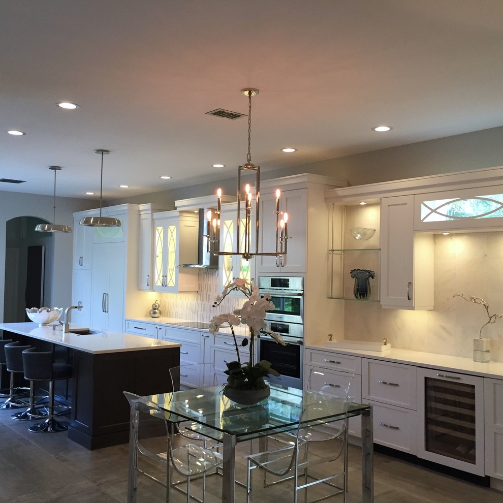 Medium sized traditional galley kitchen/diner in Miami with a built-in sink, raised-panel cabinets, white cabinets, white splashback, white appliances, a breakfast bar, brown floors and engineered stone countertops.