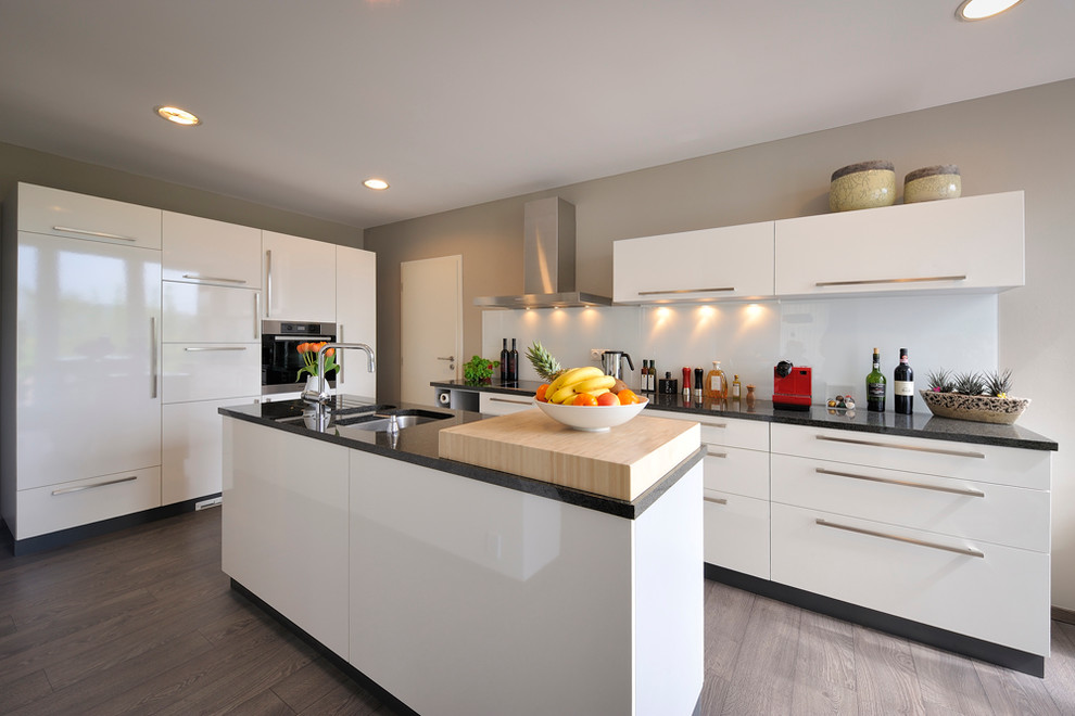 Moderne Küche mit flächenbündigen Schrankfronten, weißen Schränken, Küchenrückwand in Weiß, Glasrückwand und Elektrogeräten mit Frontblende in Sonstige