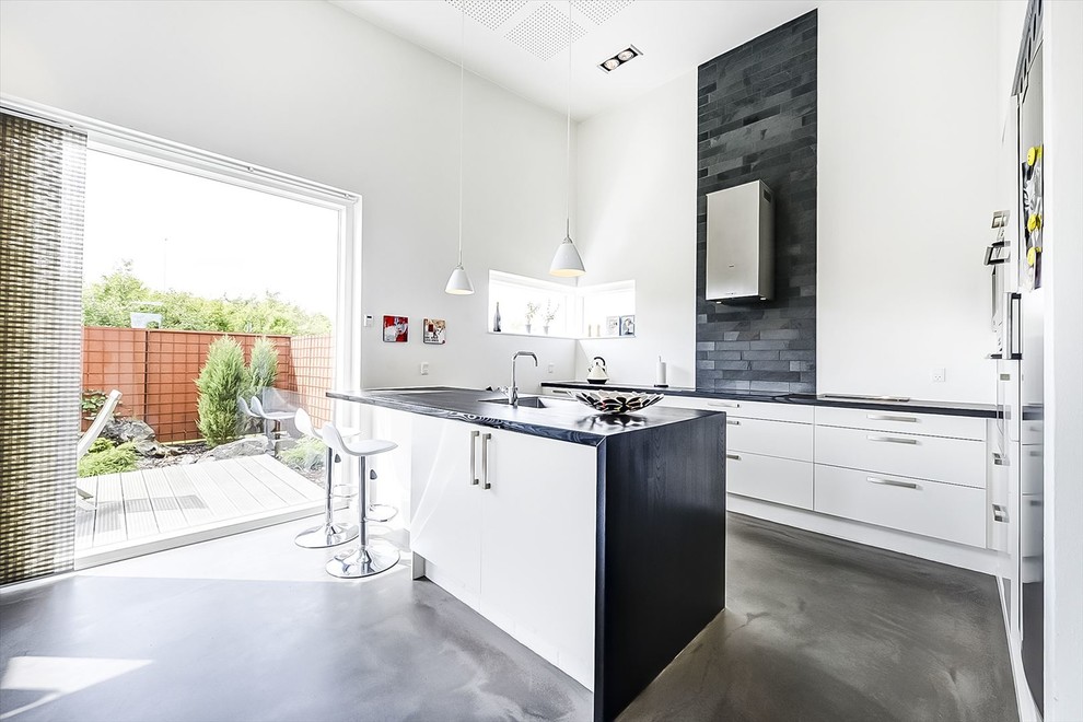 Inspiration for a large contemporary galley concrete floor open concept kitchen remodel in Aarhus with a drop-in sink, flat-panel cabinets, granite countertops, black backsplash, stone tile backsplash and an island