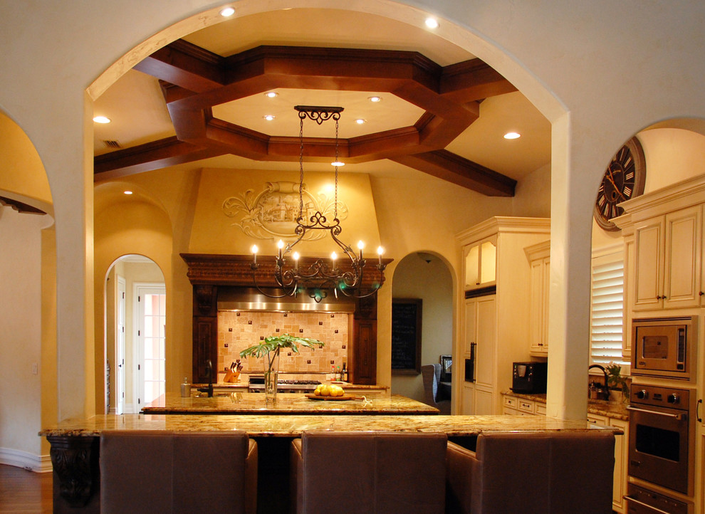 Example of a large tuscan l-shaped medium tone wood floor open concept kitchen design in Orlando with a double-bowl sink, raised-panel cabinets, white cabinets, granite countertops, beige backsplash, mosaic tile backsplash, stainless steel appliances and two islands