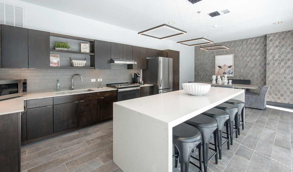 Inspiration for a classic kitchen/diner in Nashville with a submerged sink, flat-panel cabinets, dark wood cabinets, grey splashback, stainless steel appliances, medium hardwood flooring, an island, grey floors, white worktops and a feature wall.