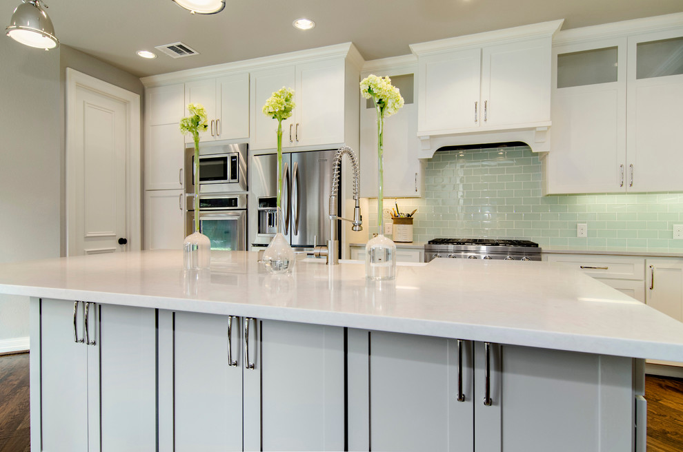 Example of a mid-sized transitional l-shaped medium tone wood floor eat-in kitchen design in Dallas with a farmhouse sink, shaker cabinets, white cabinets, granite countertops, glass tile backsplash and stainless steel appliances
