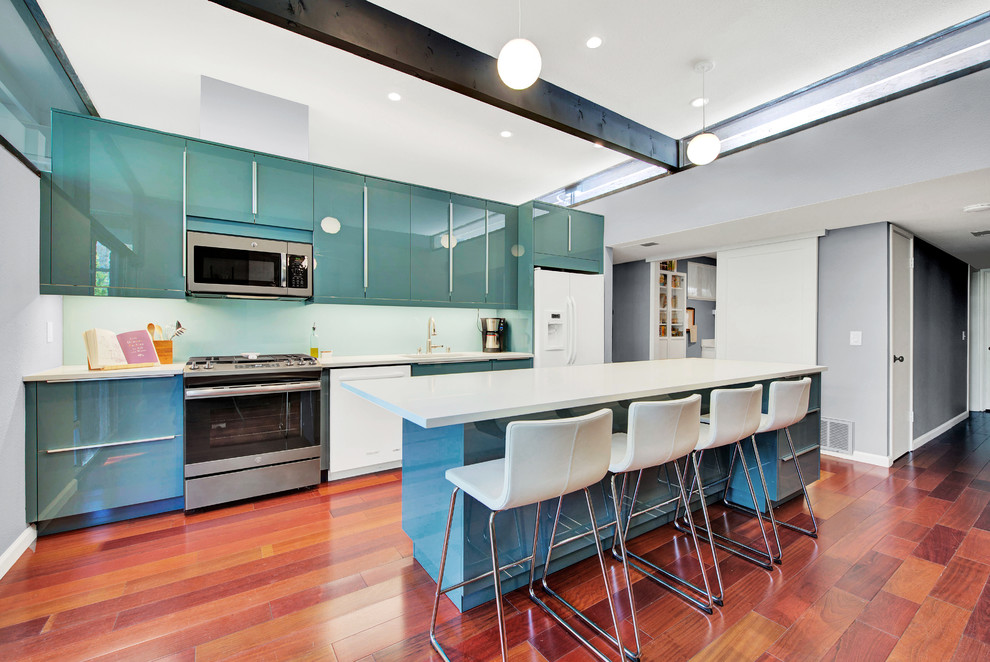 This is an example of a medium sized contemporary galley kitchen in Sacramento with engineered stone countertops, glass sheet splashback, a submerged sink, flat-panel cabinets, green cabinets, green splashback, white appliances, medium hardwood flooring, an island and brown floors.