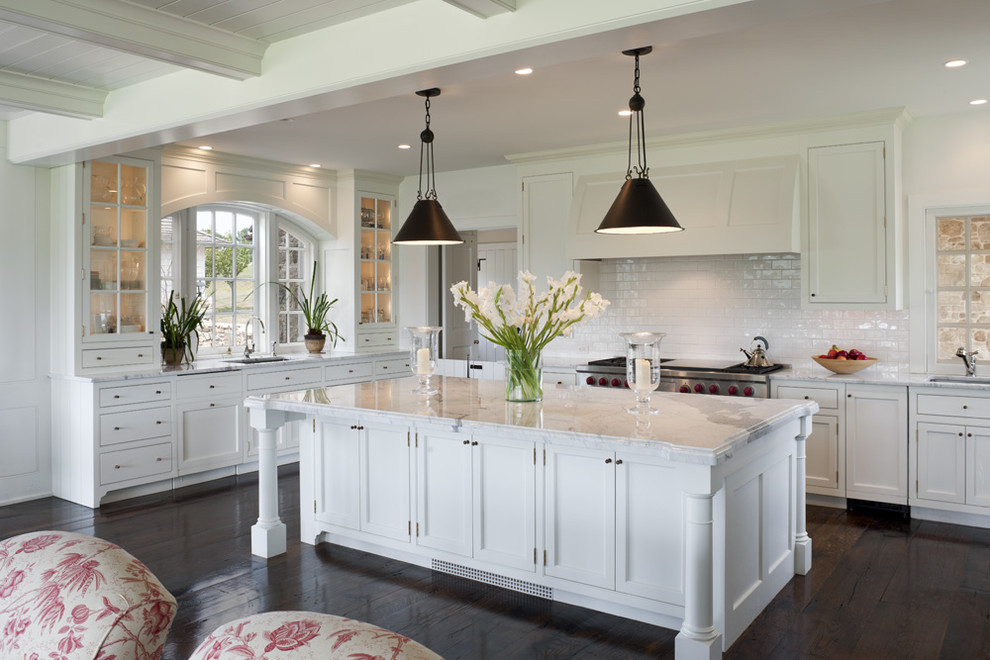 Inredning av ett klassiskt kök, med luckor med infälld panel, vita skåp, vitt stänkskydd, marmorbänkskiva, en undermonterad diskho, stänkskydd i tunnelbanekakel, rostfria vitvaror och mörkt trägolv