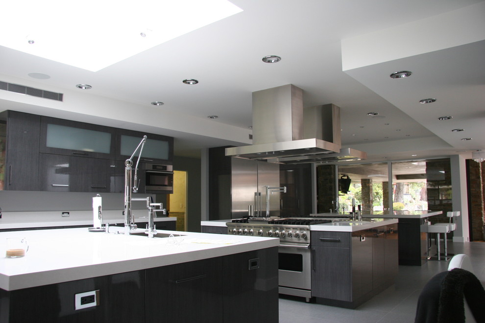 This is an example of an expansive modern kitchen in Los Angeles with a submerged sink, glass-front cabinets, grey cabinets, engineered stone countertops, stainless steel appliances and multiple islands.
