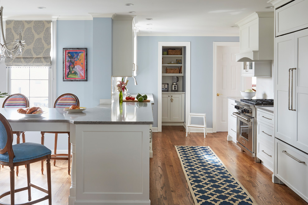 Klassisk inredning av ett kök och matrum, med luckor med infälld panel, vita skåp, vitt stänkskydd, rostfria vitvaror, mellanmörkt trägolv och brunt golv