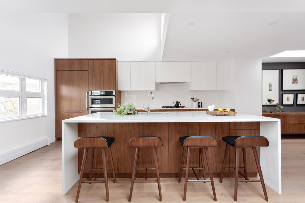 Inspiration for a contemporary galley light wood floor and beige floor kitchen remodel in Vancouver with an undermount sink, flat-panel cabinets, medium tone wood cabinets, white backsplash, paneled appliances, an island and white countertops
