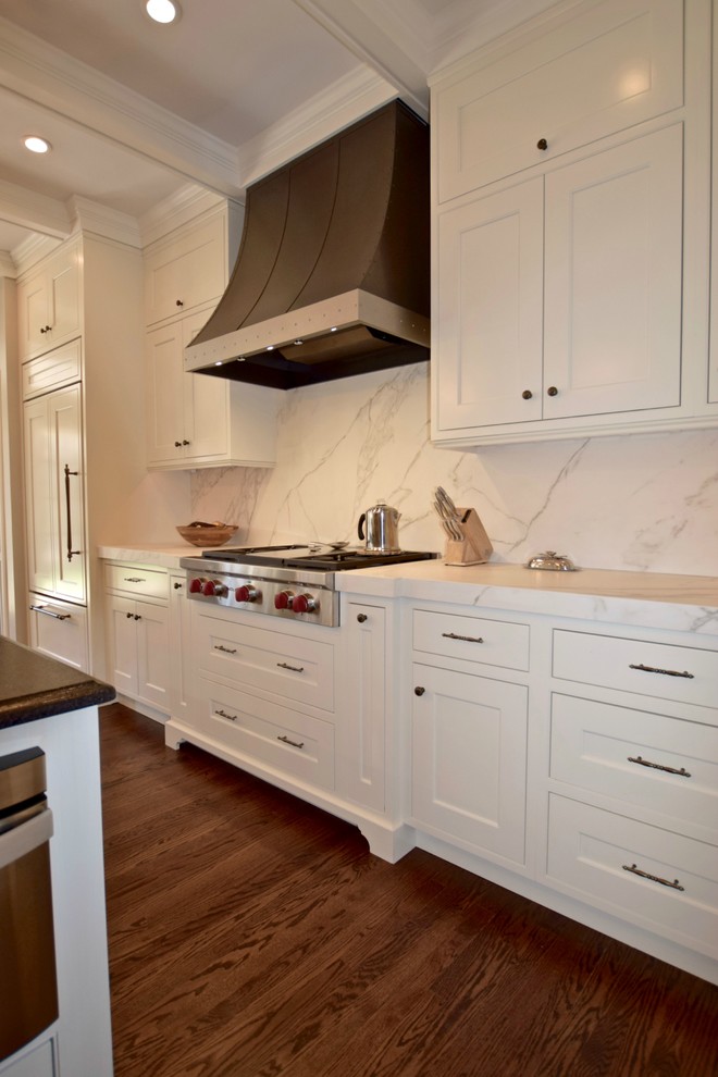 This is an example of a traditional l-shaped open plan kitchen in Denver with a submerged sink, beaded cabinets, white cabinets, white splashback, stone slab splashback, stainless steel appliances, medium hardwood flooring and an island.