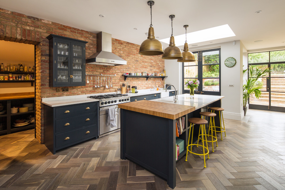 Inspiration for a country galley open plan kitchen in London with a belfast sink, glass-front cabinets, blue cabinets, brick splashback, stainless steel appliances, medium hardwood flooring and an island.