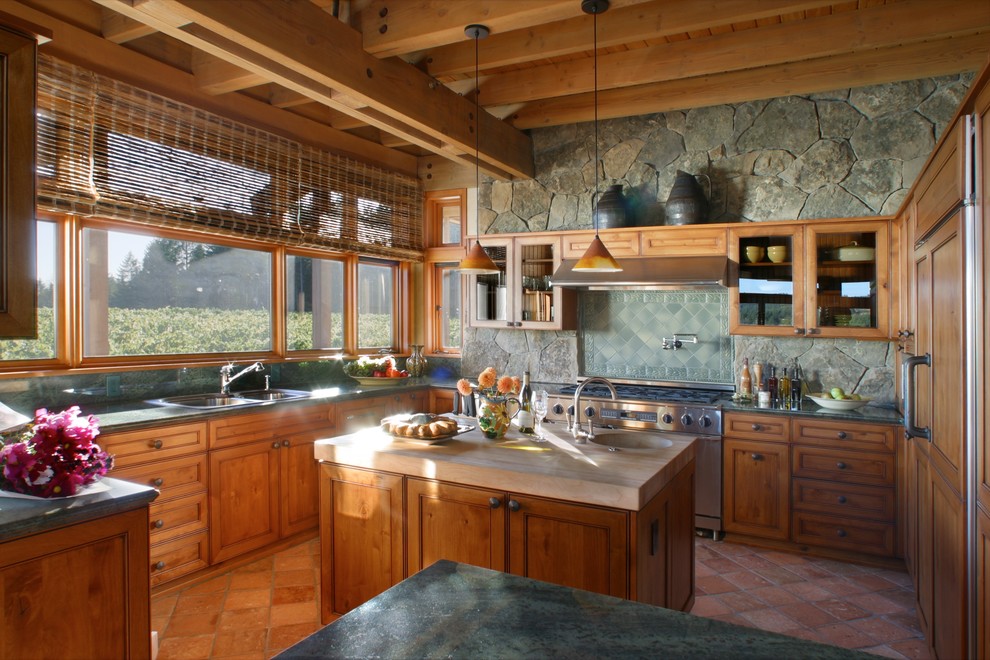 Inspiration för mellanstora amerikanska kök, med en dubbel diskho, luckor med infälld panel, skåp i mellenmörkt trä, bänkskiva i koppar, grönt stänkskydd, stänkskydd i stenkakel, rostfria vitvaror, klinkergolv i terrakotta, en köksö och brunt golv