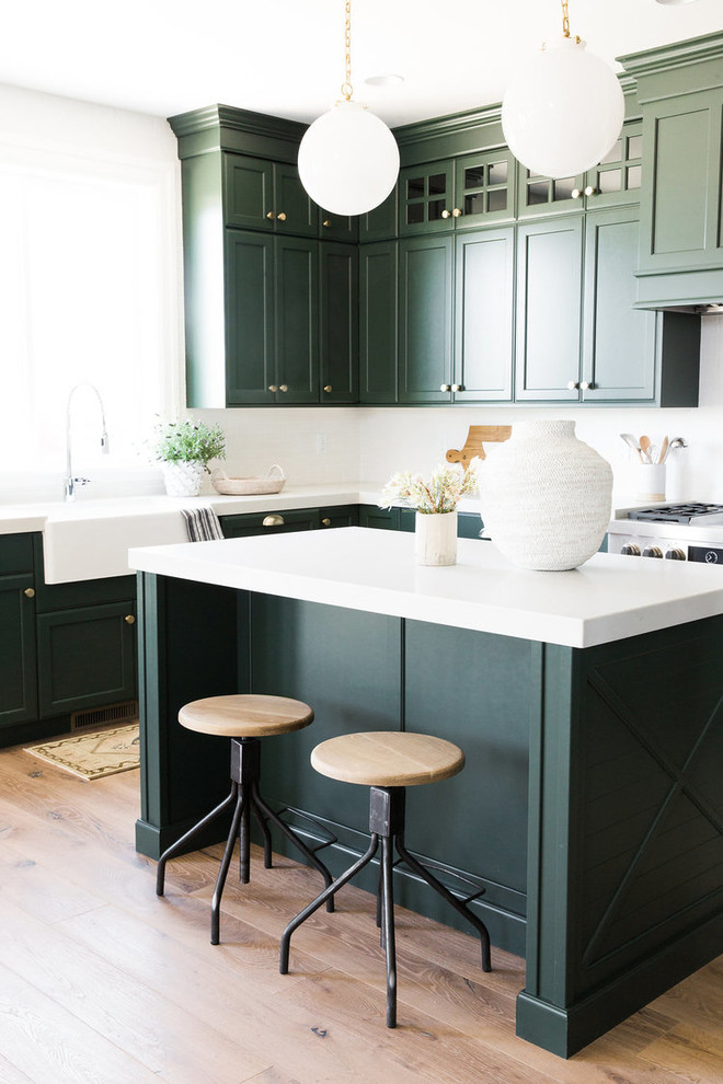 Medium sized traditional kitchen/diner in Salt Lake City with a belfast sink, green cabinets, white splashback, stainless steel appliances, medium hardwood flooring and an island.