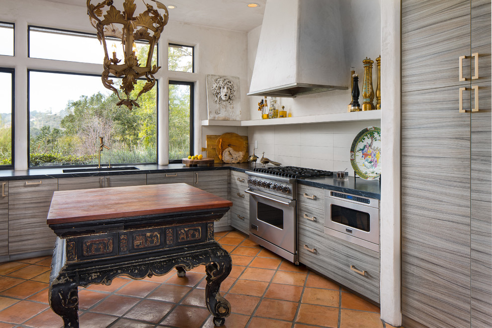 Inspiration for a mid-sized eclectic u-shaped terra-cotta tile kitchen remodel in San Francisco with flat-panel cabinets, gray cabinets, solid surface countertops, gray backsplash, subway tile backsplash, stainless steel appliances, an island and an undermount sink