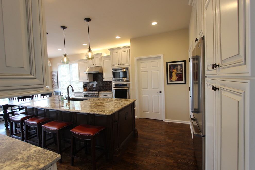 Example of a classic u-shaped dark wood floor open concept kitchen design in Atlanta with a single-bowl sink, raised-panel cabinets, distressed cabinets, granite countertops, brown backsplash, glass tile backsplash, stainless steel appliances and no island