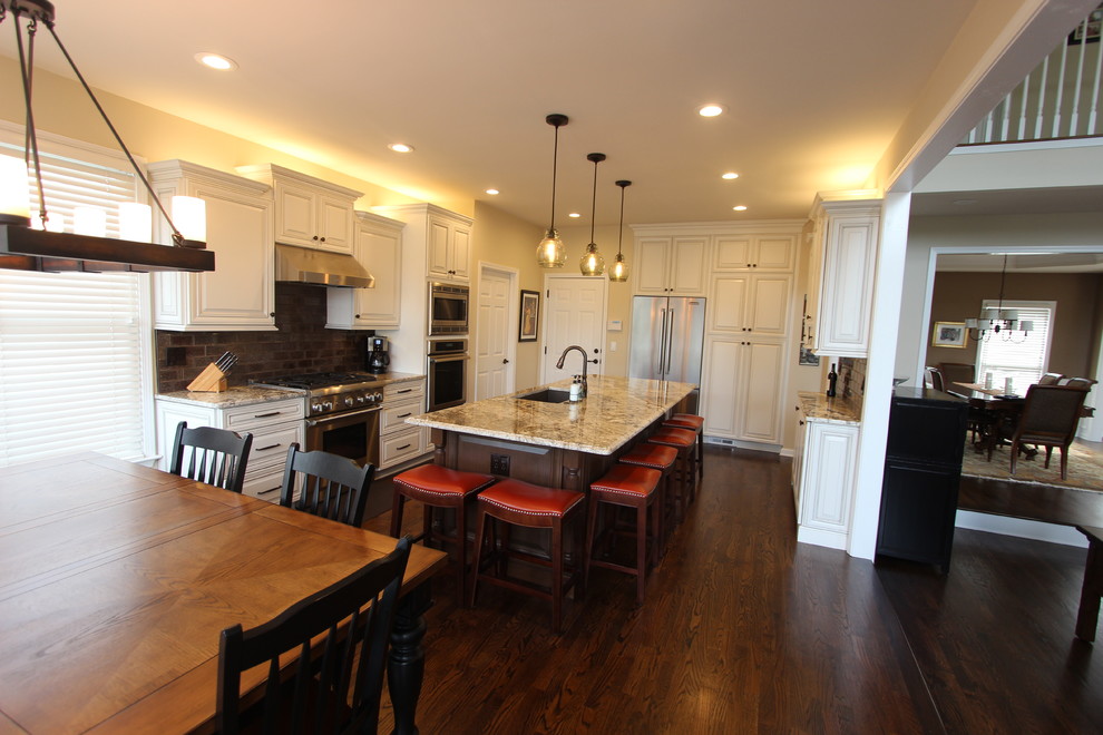 Example of a large classic u-shaped dark wood floor open concept kitchen design in Atlanta with a single-bowl sink, raised-panel cabinets, distressed cabinets, granite countertops, brown backsplash, glass tile backsplash, stainless steel appliances and an island