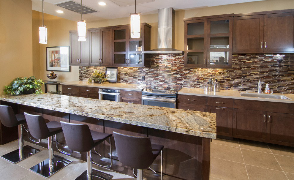 This is an example of a large contemporary galley kitchen/diner in Las Vegas with recessed-panel cabinets, dark wood cabinets, marble worktops, brown splashback, mosaic tiled splashback, stainless steel appliances and an island.