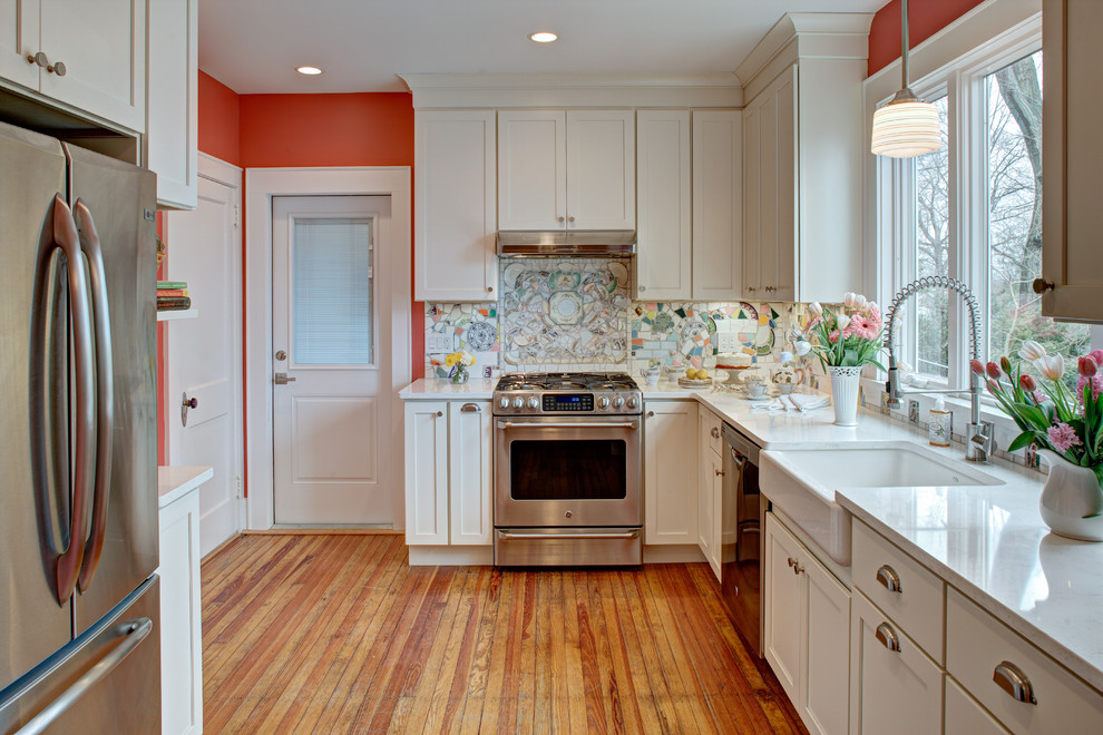 Inspiration for a mid-sized eclectic medium tone wood floor enclosed kitchen remodel in New York with a farmhouse sink, shaker cabinets, white cabinets, quartz countertops, multicolored backsplash, stainless steel appliances and no island