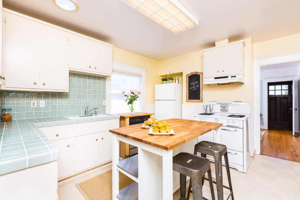 Photo of a small traditional u-shaped enclosed kitchen in San Francisco with flat-panel cabinets, white cabinets, tile countertops, blue splashback, ceramic splashback, white appliances, an island and turquoise worktops.