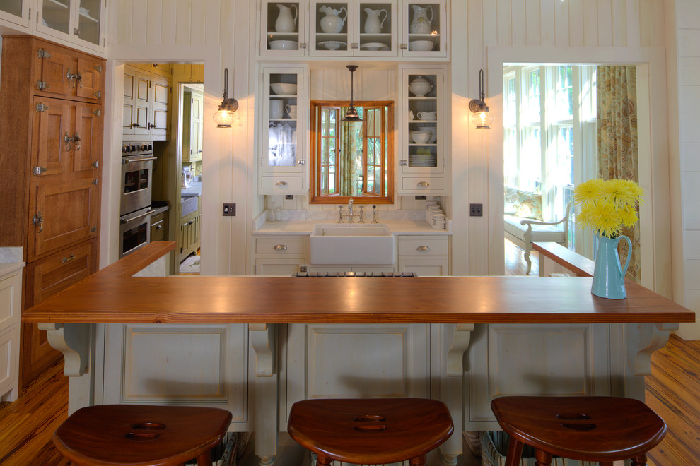 Bild på ett avskilt, mellanstort maritimt parallellkök, med en rustik diskho, luckor med infälld panel, träbänkskiva, vitt stänkskydd, rostfria vitvaror, vita skåp, mellanmörkt trägolv och en köksö