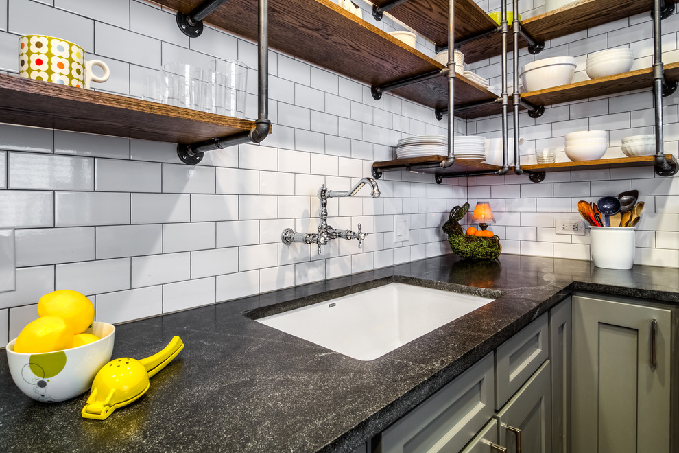 This is an example of a small industrial galley enclosed kitchen in Boston with a submerged sink, shaker cabinets, grey cabinets, granite worktops, white splashback, metro tiled splashback, white appliances, ceramic flooring, no island and brown floors.