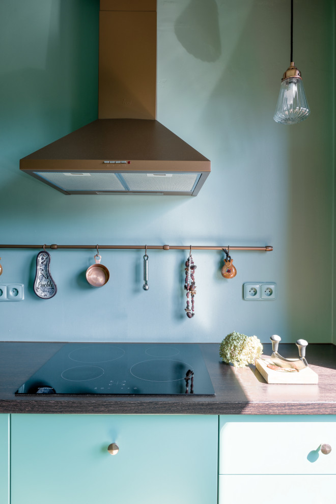 Immagine di una cucina minimalista di medie dimensioni con lavello integrato, ante lisce, ante verdi, top in legno, paraspruzzi verde, elettrodomestici neri, pavimento in cementine, penisola, pavimento verde e top marrone
