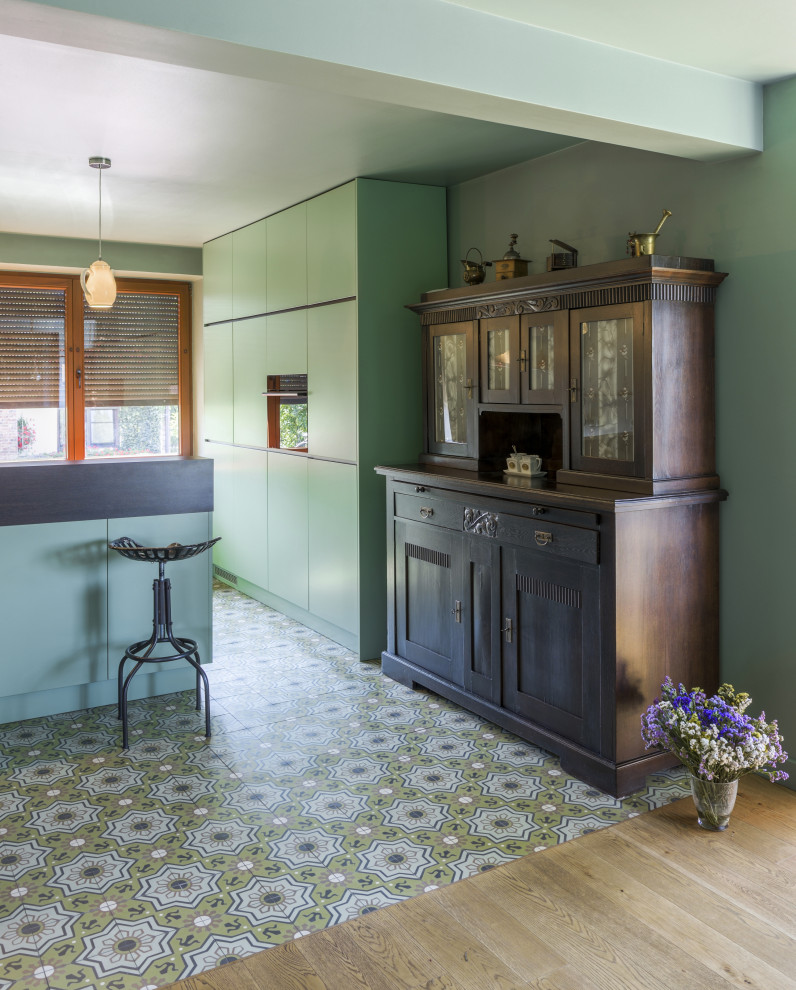 ロンドンにある高級な中くらいなエクレクティックスタイルのおしゃれなキッチン (一体型シンク、フラットパネル扉のキャビネット、緑のキャビネット、木材カウンター、緑のキッチンパネル、黒い調理設備、セメントタイルの床、緑の床、茶色いキッチンカウンター) の写真