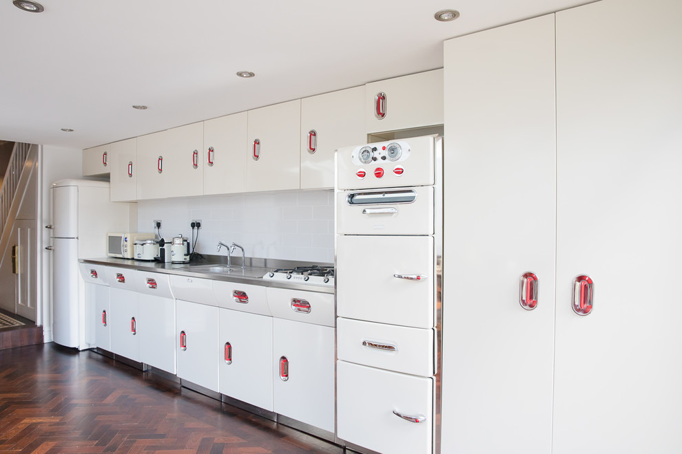 Foto di una grande cucina industriale con ante bianche, top in acciaio inossidabile, pavimento in legno massello medio, pavimento marrone e top grigio
