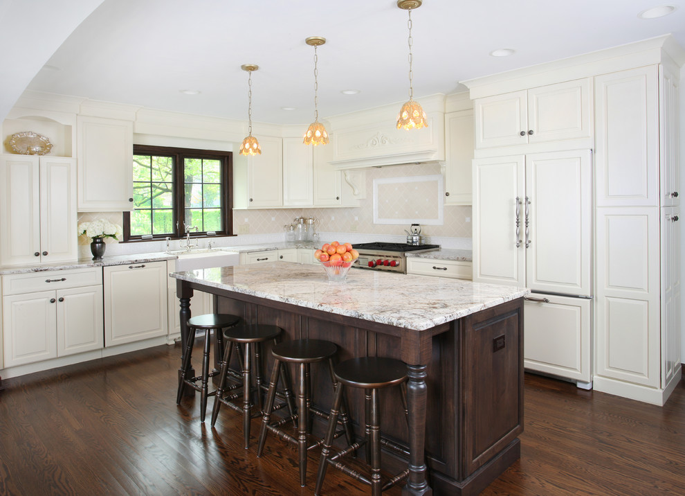 Kitchen - large traditional l-shaped dark wood floor kitchen idea in Chicago with raised-panel cabinets, white cabinets, beige backsplash, paneled appliances, an island, a farmhouse sink, granite countertops and ceramic backsplash