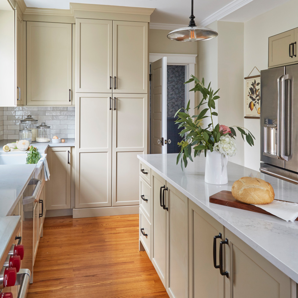 Inspiration for a timeless u-shaped medium tone wood floor enclosed kitchen remodel in Chicago with a farmhouse sink, shaker cabinets, beige cabinets, quartzite countertops, white backsplash, porcelain backsplash, stainless steel appliances, an island and beige countertops