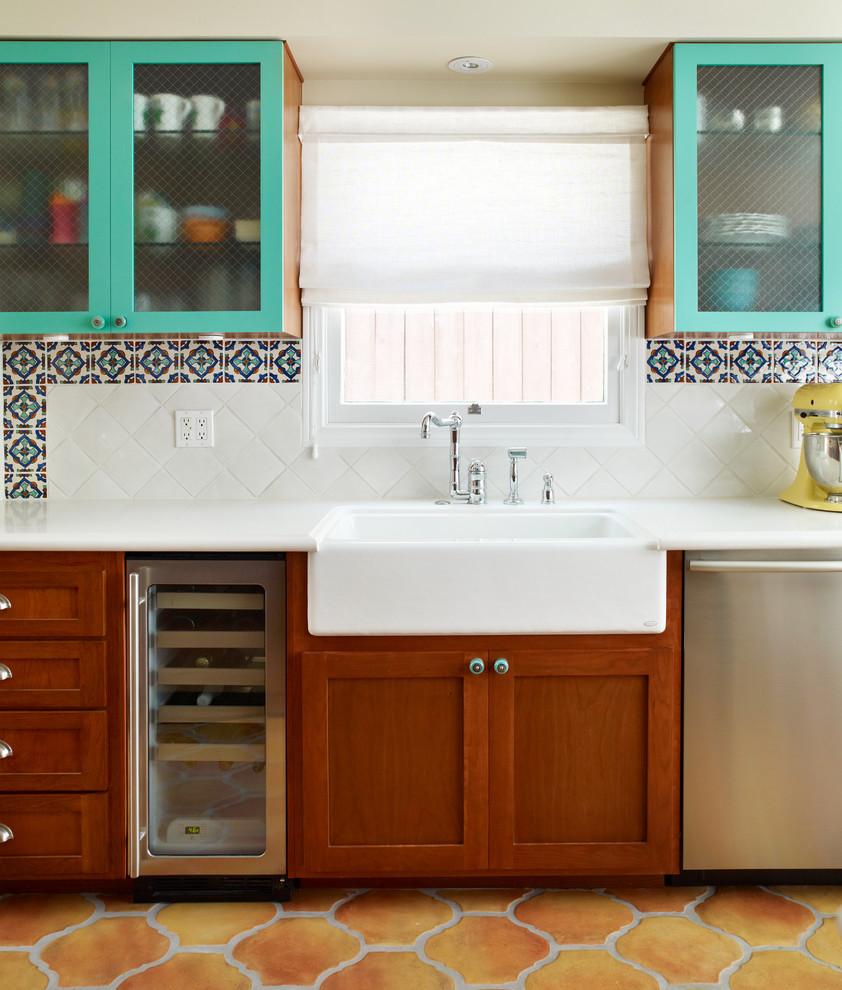 Cette image montre une cuisine traditionnelle avec un placard à porte vitrée, un électroménager en acier inoxydable, un évier de ferme, des portes de placard bleues, une crédence multicolore et tomettes au sol.