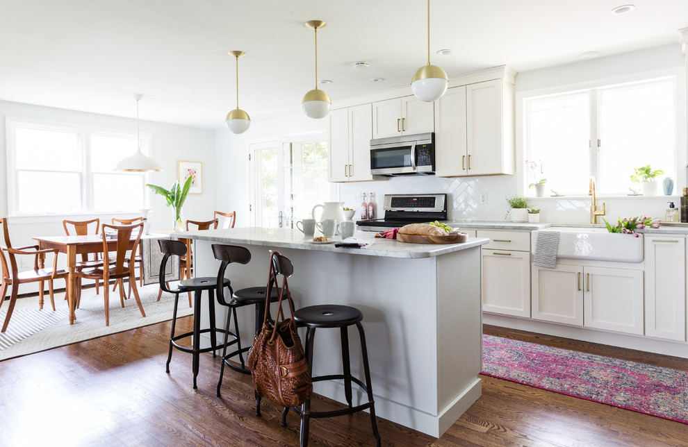 Kitchen - mid-sized modern l-shaped medium tone wood floor and brown floor kitchen idea in Philadelphia with a farmhouse sink, shaker cabinets, white cabinets, quartzite countertops, white backsplash, ceramic backsplash, stainless steel appliances and an island