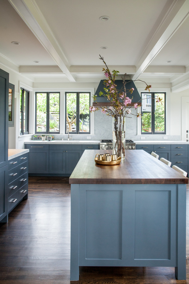 Modern inredning av ett stort kök, med grått stänkskydd, mörkt trägolv, en köksö, brunt golv, en undermonterad diskho, luckor med infälld panel, träbänkskiva, rostfria vitvaror och blå skåp