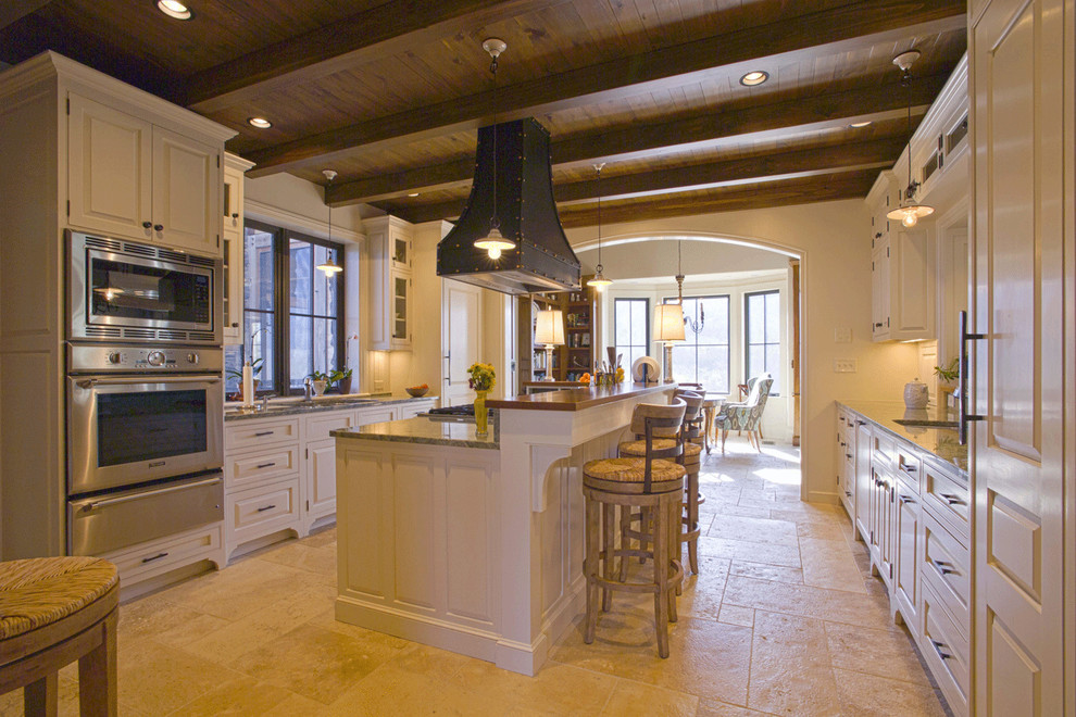 Foto på ett stort amerikanskt kök, med en undermonterad diskho, luckor med upphöjd panel, granitbänkskiva, flerfärgad stänkskydd, rostfria vitvaror, kalkstensgolv, vita skåp och en köksö