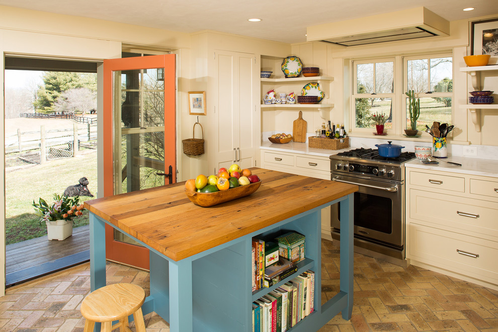 Idéer för att renovera ett mellanstort lantligt kök, med en rustik diskho, luckor med infälld panel, blå skåp, träbänkskiva, rostfria vitvaror, tegelgolv och en köksö
