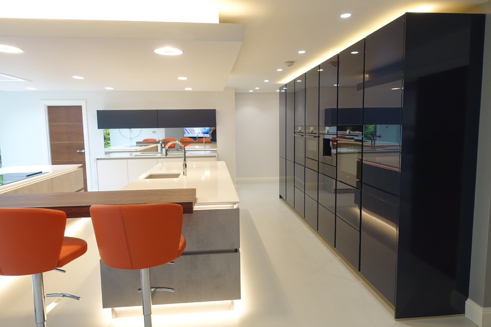 Expansive modern galley open plan kitchen in Surrey with an integrated sink, flat-panel cabinets, grey cabinets, granite worktops, integrated appliances, multiple islands, white floors and white worktops.