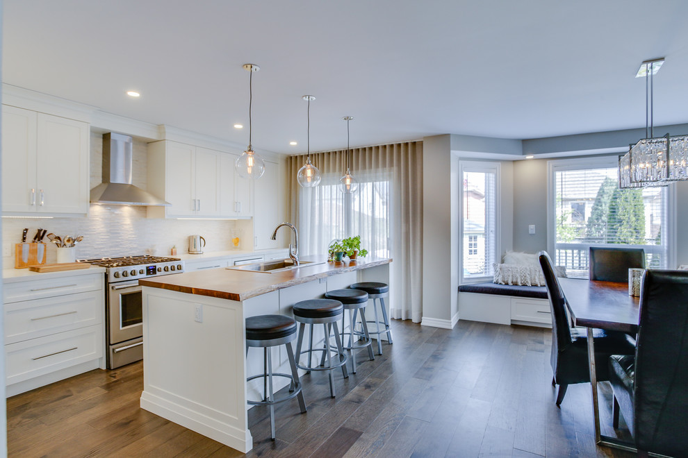 Example of a l-shaped dark wood floor and brown floor eat-in kitchen design in Toronto with a single-bowl sink, shaker cabinets, white cabinets, quartz countertops, white backsplash, marble backsplash, stainless steel appliances, an island and white countertops