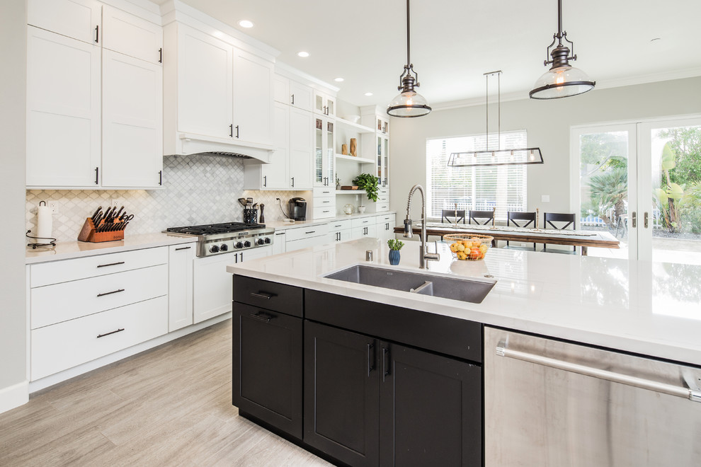 Photo of a medium sized country galley open plan kitchen in San Diego with a submerged sink, shaker cabinets, white cabinets, engineered stone countertops, beige splashback, porcelain splashback, stainless steel appliances, light hardwood flooring, an island and beige floors.
