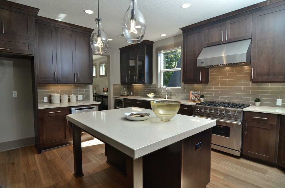 Photo of a large contemporary kitchen in Portland with recessed-panel cabinets, dark wood cabinets, engineered stone countertops, beige splashback, glass tiled splashback, stainless steel appliances, medium hardwood flooring and an island.