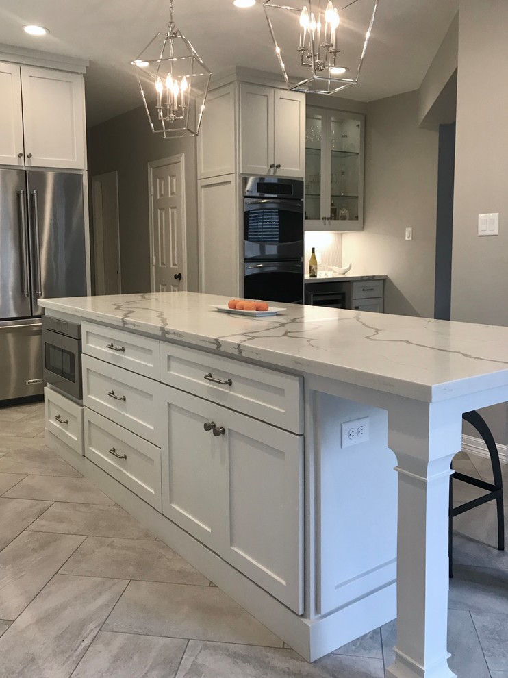 Photo of a large classic l-shaped kitchen in Houston with a submerged sink, shaker cabinets, white cabinets, engineered stone countertops, grey splashback, ceramic splashback, stainless steel appliances, porcelain flooring, an island, grey floors and white worktops.