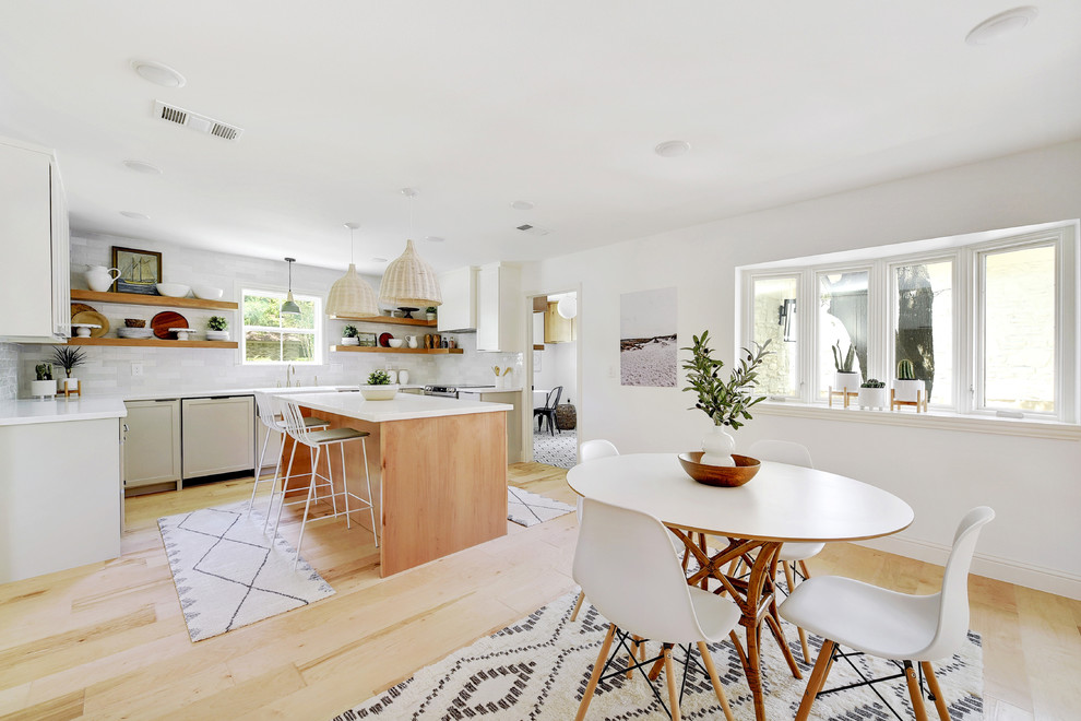 Photo of a coastal l-shaped kitchen/diner in Austin with open cabinets, white splashback, light hardwood flooring, an island and white worktops.