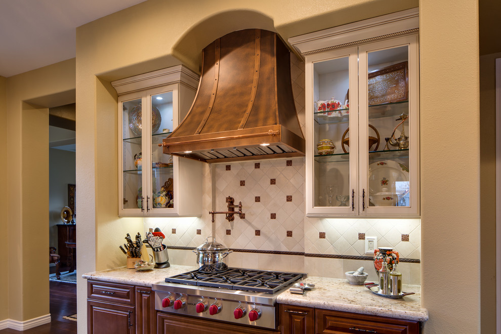 Inspiration for a large mediterranean l-shaped eat-in kitchen remodel in San Diego with raised-panel cabinets, distressed cabinets, granite countertops, white backsplash, porcelain backsplash, stainless steel appliances and an island