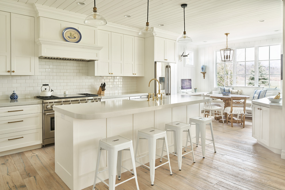 Example of a cottage galley light wood floor eat-in kitchen design in Other with a farmhouse sink, shaker cabinets, white cabinets, white backsplash, subway tile backsplash, stainless steel appliances and an island
