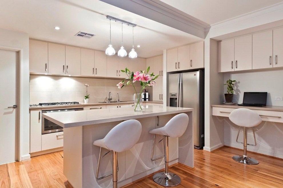 Medium sized contemporary l-shaped kitchen/diner in Perth with stainless steel appliances, a built-in sink, beige cabinets, engineered stone countertops, beige splashback, ceramic splashback, medium hardwood flooring and an island.