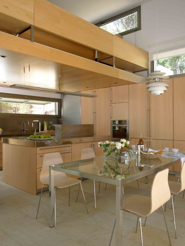 Exempel på ett mellanstort minimalistiskt kök, med släta luckor, skåp i mellenmörkt trä, bänkskiva i rostfritt stål, stänkskydd med metallisk yta, rostfria vitvaror, kalkstensgolv och en halv köksö