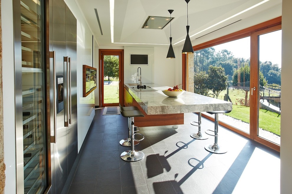 Cette image montre une grande cuisine américaine parallèle design en bois brun avec un évier 2 bacs, un placard à porte plane, plan de travail en marbre, un électroménager en acier inoxydable, un sol en ardoise et une péninsule.