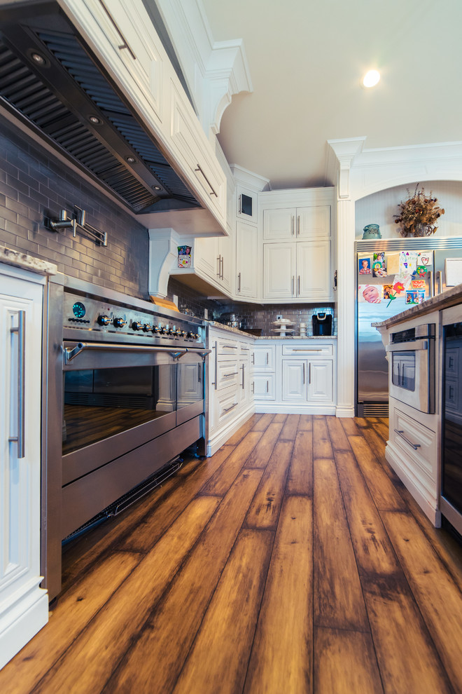 Inspiration for a large country u-shaped enclosed kitchen in Sacramento with a belfast sink, raised-panel cabinets, white cabinets, granite worktops, metallic splashback, metal splashback, stainless steel appliances, dark hardwood flooring, an island, brown floors and brown worktops.