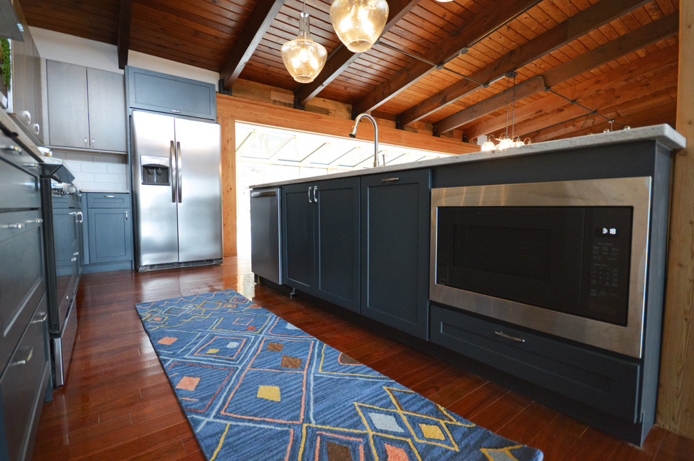 Example of a mid-sized urban u-shaped dark wood floor and red floor open concept kitchen design in Other with an undermount sink, shaker cabinets, blue cabinets, granite countertops, white backsplash, subway tile backsplash, stainless steel appliances, an island and white countertops