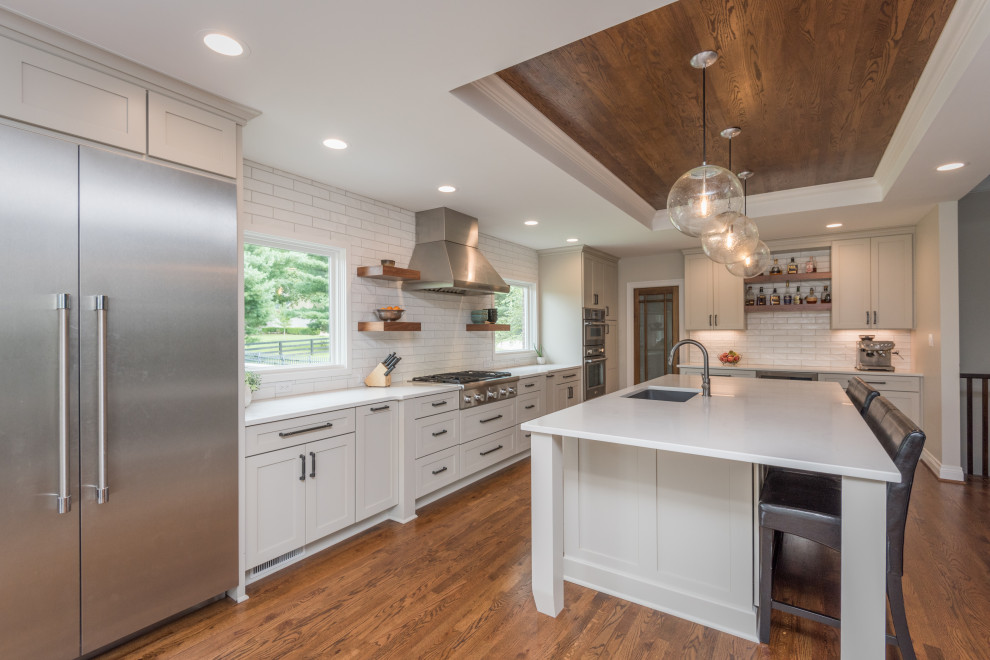 Kitchen - transitional l-shaped dark wood floor, brown floor, tray ceiling and wood ceiling kitchen idea in Louisville with an undermount sink, shaker cabinets, white cabinets, white backsplash, stainless steel appliances, an island and white countertops